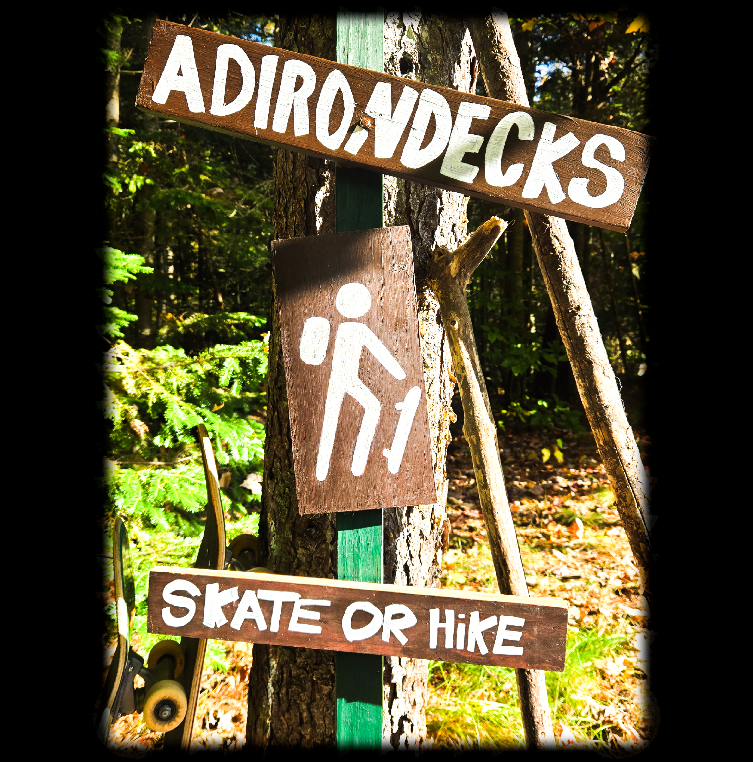 Wooden sign on a tree in a forest with 'Adirondecks' and 'Skate or Hike' text.